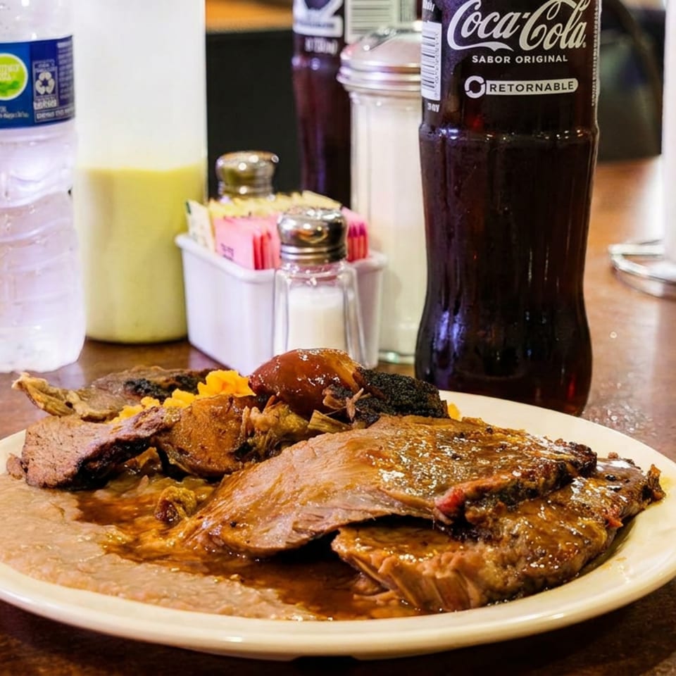 Braised beef with beans, watermelon, and drinks on a restaurant table with condiments.
