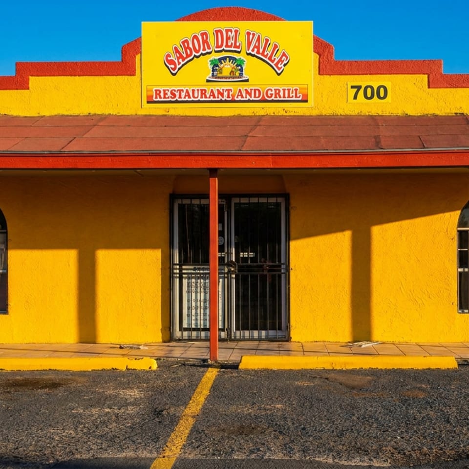 Bright yellow Sabor Del Valle Restaurant and Grill building with red trim, arched windows, and a parking lot.