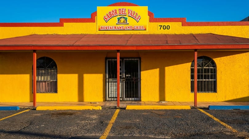 Bright yellow Sabor Del Valle Restaurant and Grill building with red trim, arched windows, and a parking lot.